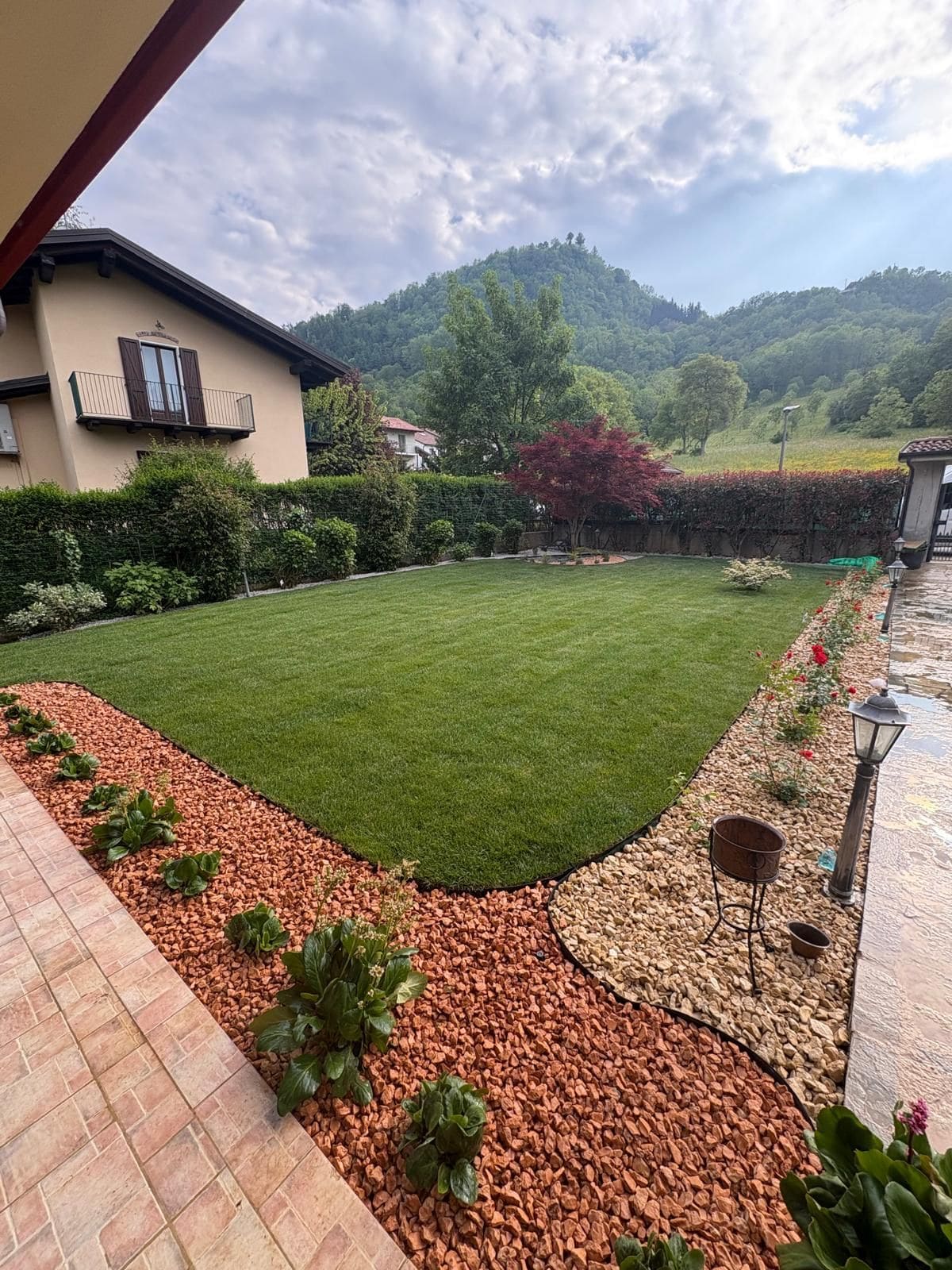 Prato all'inglese con bordure in ghiaia rossa e piante, con le colline sullo sfondo
