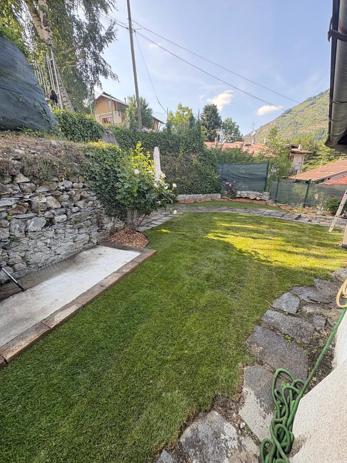 Prato lungo un muro di pietra con vialetto e aiuola curata