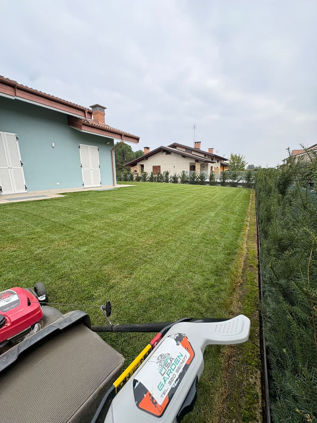 Prato tagliato a strisce accanto a una casa, con il tosaerba di Lisa Garden in primo piano