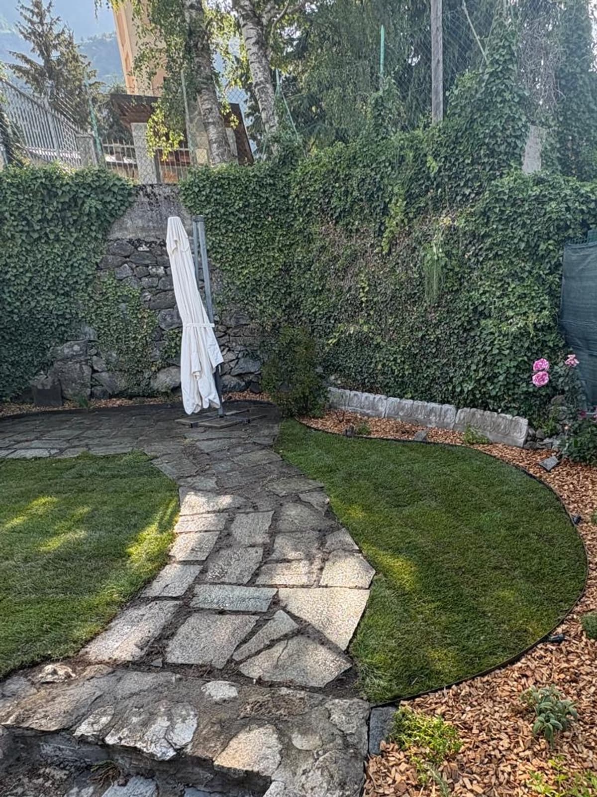 Prato nuovo, vialetto in pietra e scalini con bordura in corteccia in un giardino di montagna