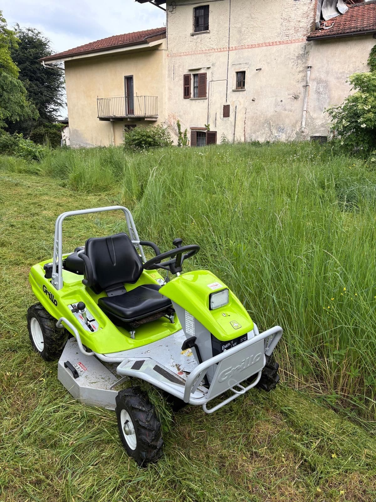 Trattorino trinciaerba verde in un prato di erba alta davanti a una casa