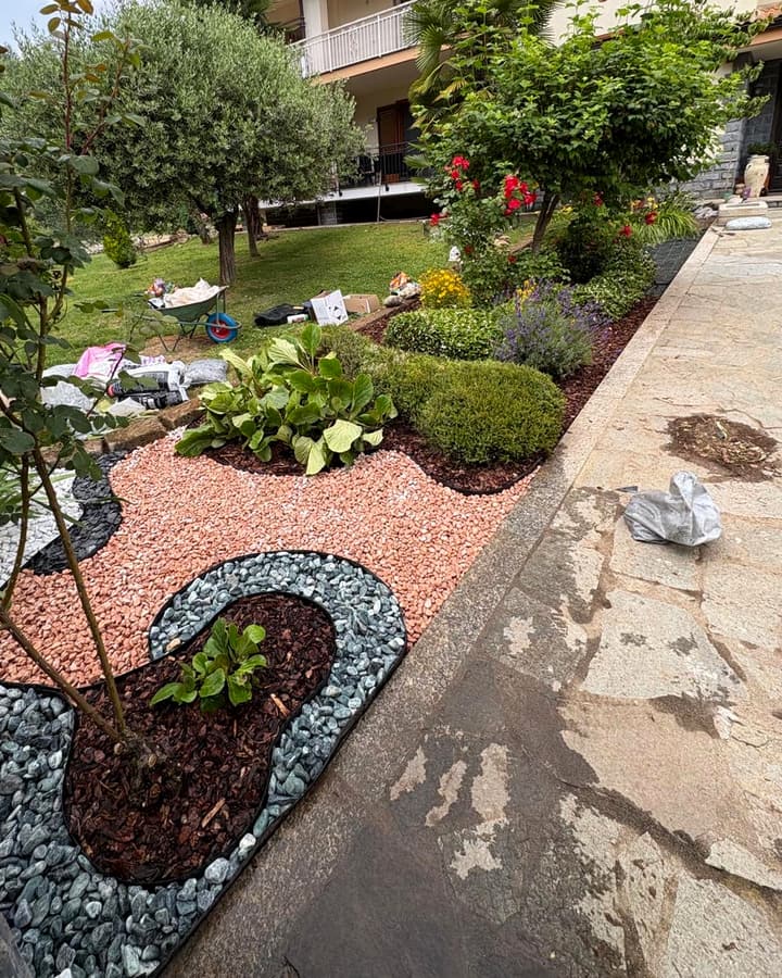 Dopo: aiuola con ghiaia decorativa rosa, bianca, nera e verde disegnata a curve, bordure scure e corteccia attorno alle piante